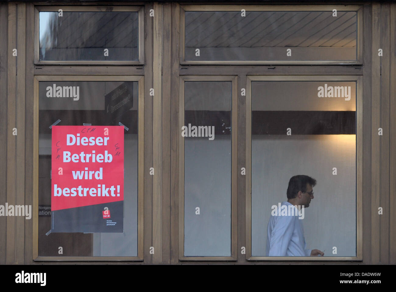 A man walks past a poster lettered 'Dieser Btrieb wird bestreikt' ('This company is on strike') fixed to a door of the Charite in Berlin, Germany, 02 November 2011. Around 200 staff members of the subsidiary Facility Management call for a wage agreement for eight weeks now.   Photo: SOEREN STACHE Stock Photo