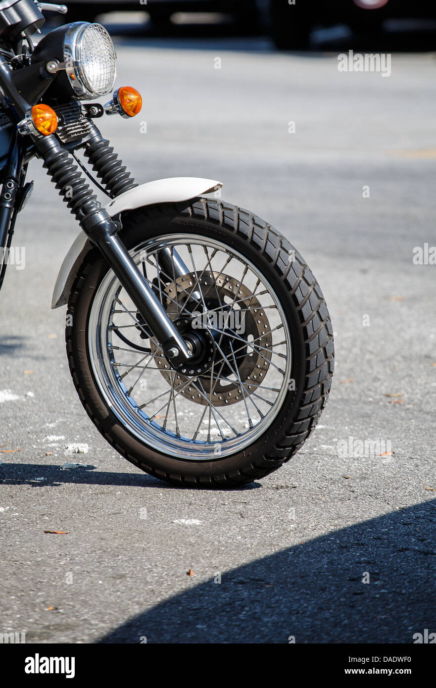 The front wheel of a motorcyle parked in the street showing brakes and spokes Stock Photo