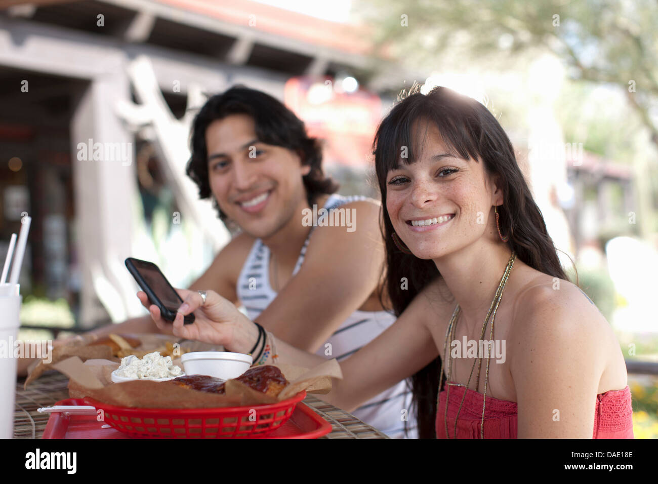 Young woman holding mobile phone in outdoor cafe, smiling Stock Photo