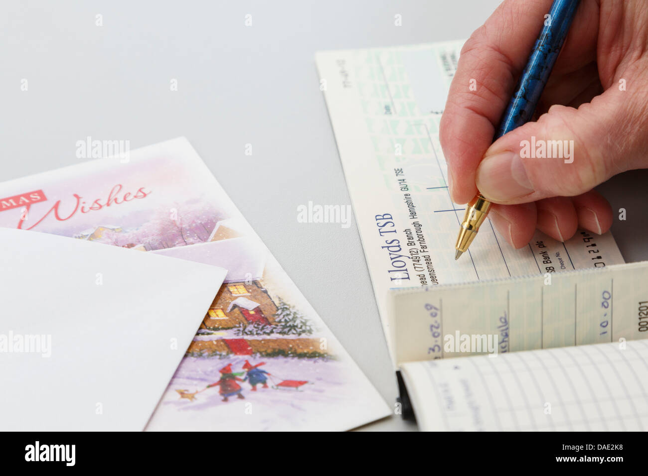 Senior female lady pensioner writing a Lloyds bank cheque as a gift to put in a Christmas card. England, UK, Britain. Stock Photo