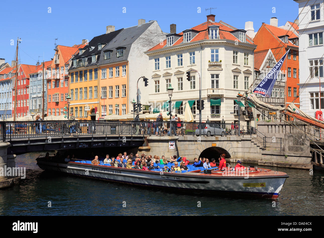 Tourists on canal tour boat passing under low bridge with colourful buildings in Nyhavn harbour, Copenhagen, Zealand, Denmark Stock Photo