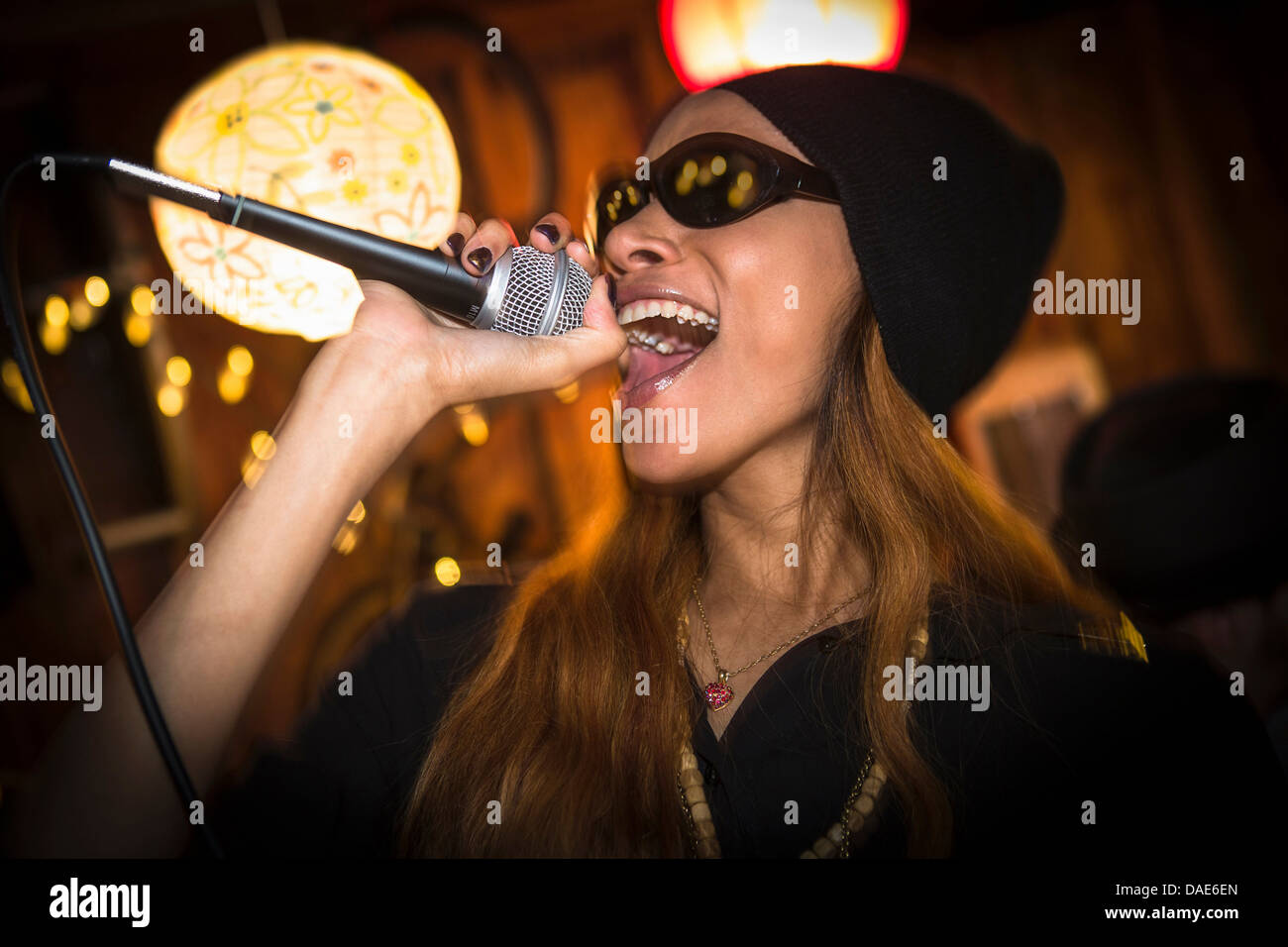 Woman wearing hat and sunglasses singing in microphone Stock Photo