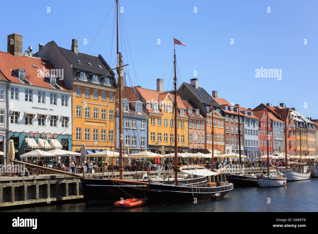 Old wooden boats moored by canal quay with colourful 17th century buildings on waterfront in Nyhavn harbour, Copenhagen, Denmark Stock Photo