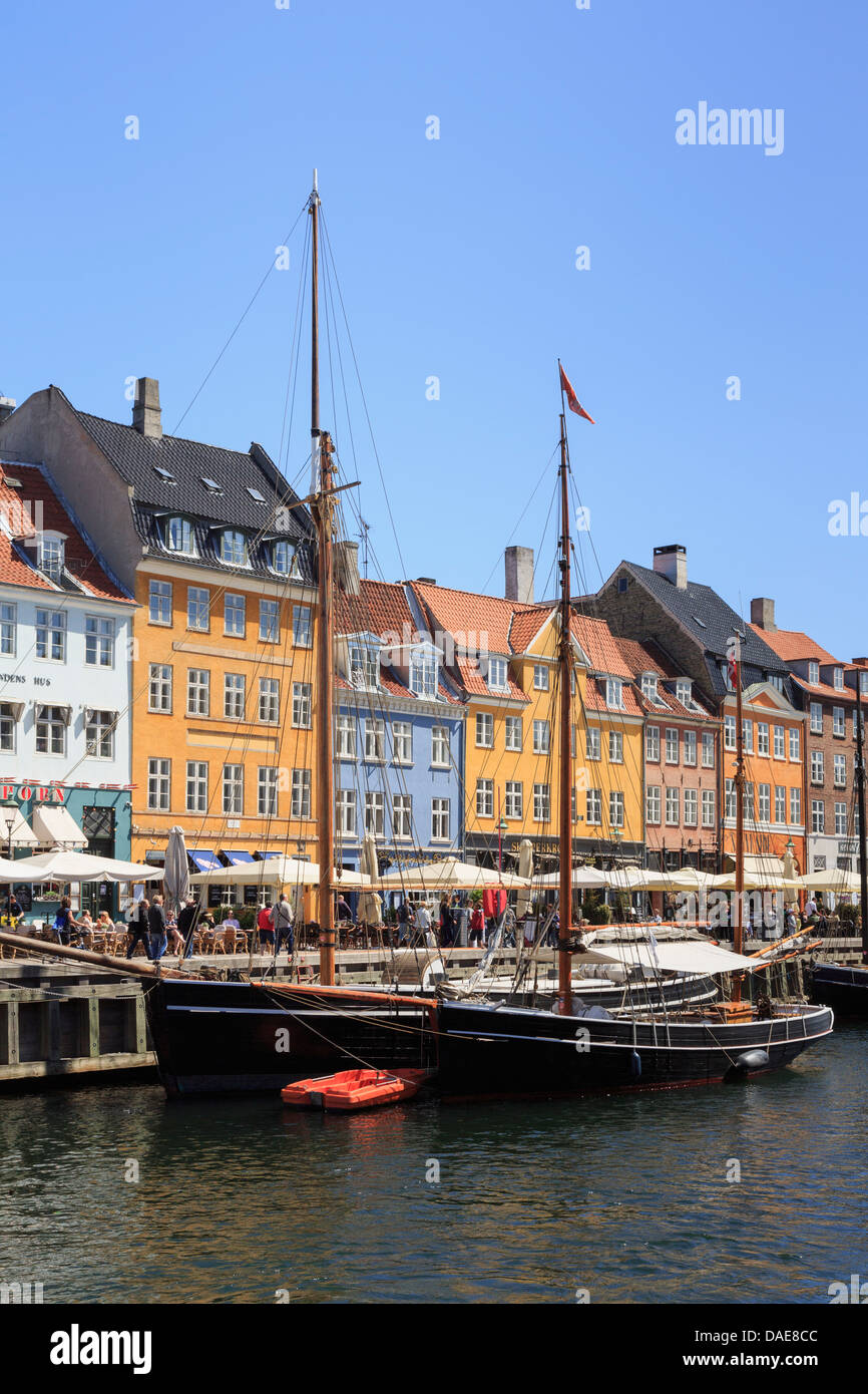 Old wooden boats moored on canal quay with colourful 17th century buildings on waterfront in Nyhavn harbour, Copenhagen, Denmark Stock Photo