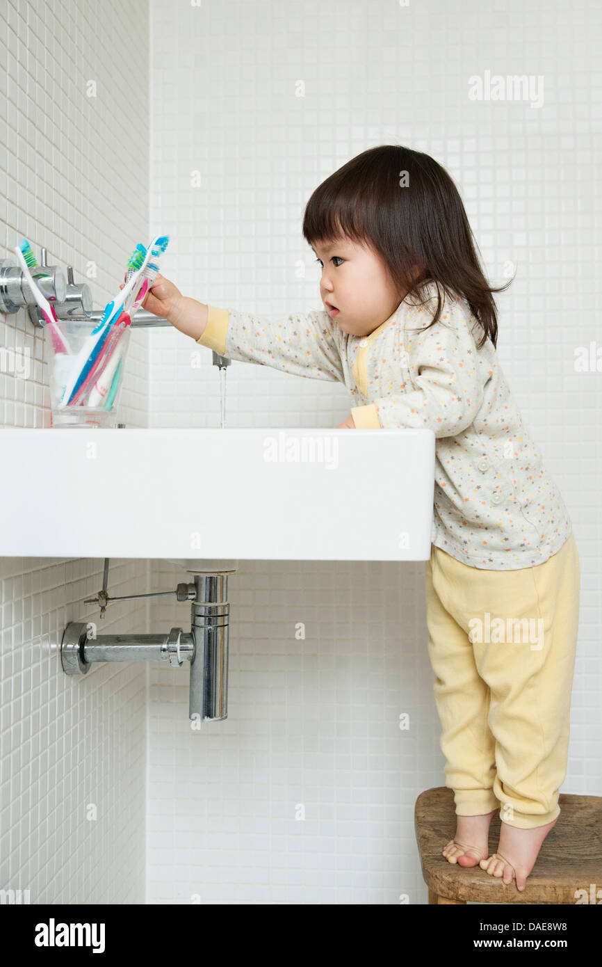 Girl toddler on tiptoe reaching over bathroom sink Stock Photo