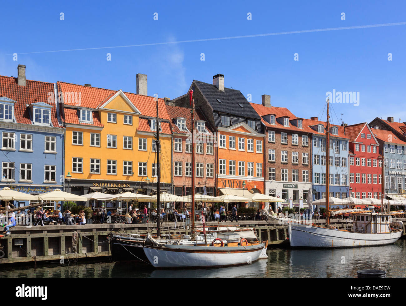 Wooden boats moored on canal with cafes and colourful buildings on waterfront in Nyhavn harbour Copenhagen Zealand Denmark Stock Photo