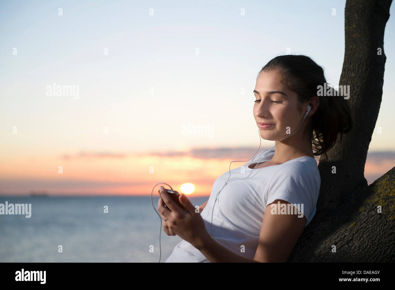 Close up of young woman leaning on tree at dusk Stock Photo