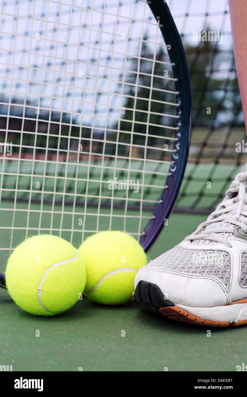 Tennis shoe, racket and balls on a hard court in front of net. Stock Photo