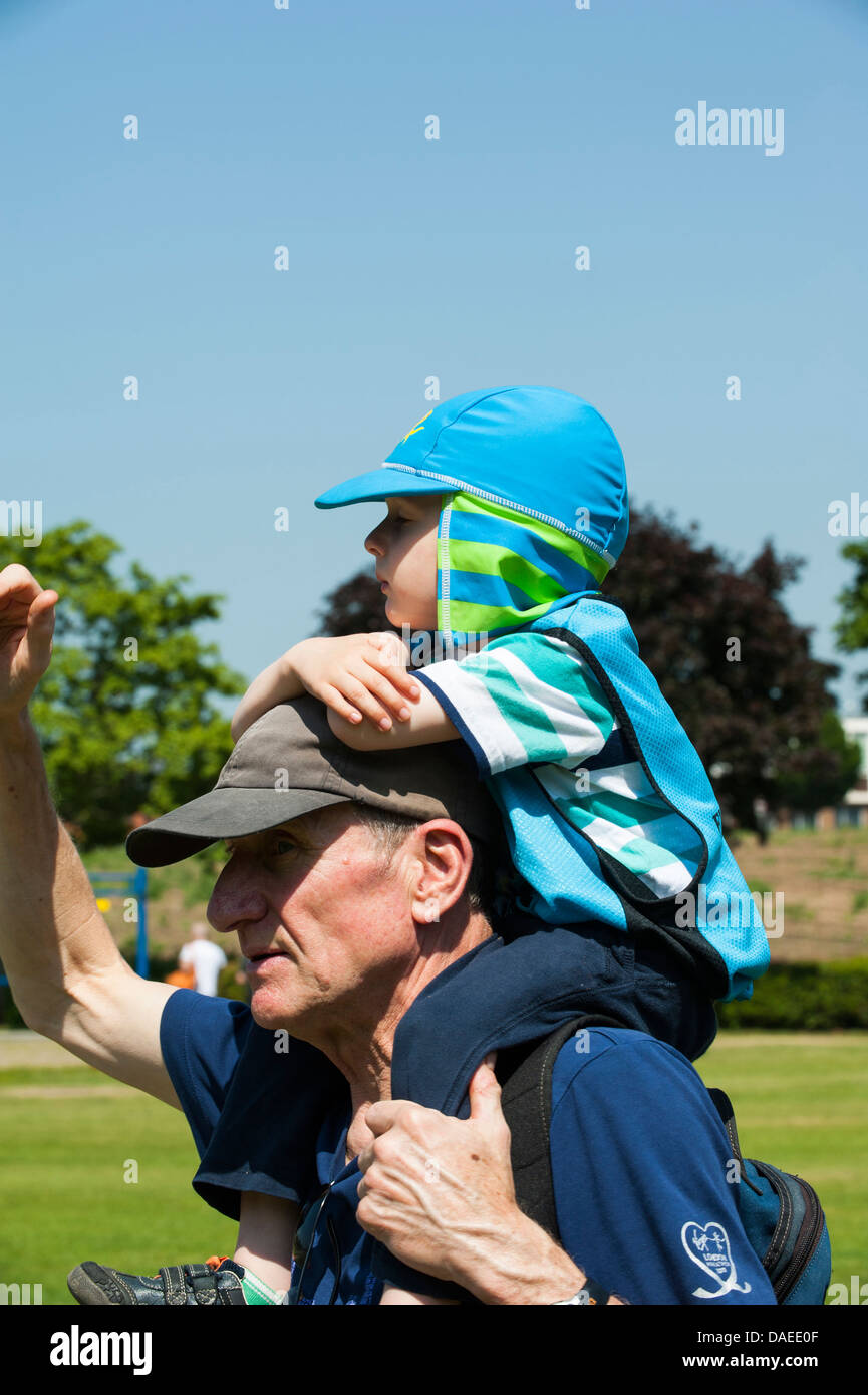 Young boy sits on shoulders of elderly man both wear protective head