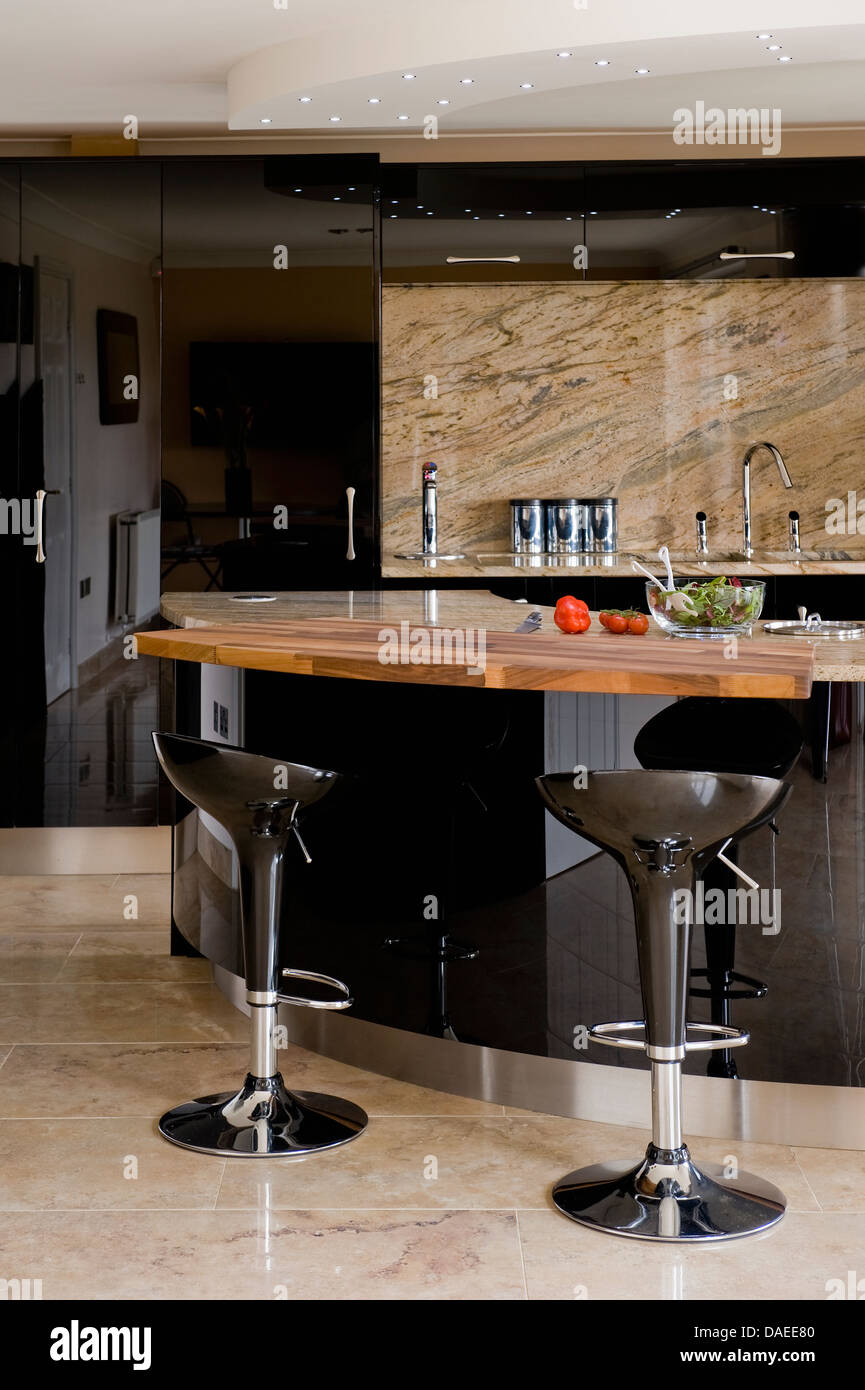 Pair of black Bombo bar stools at black breakfast bar in modern kitchen with polished granite splash-back Stock Photo
