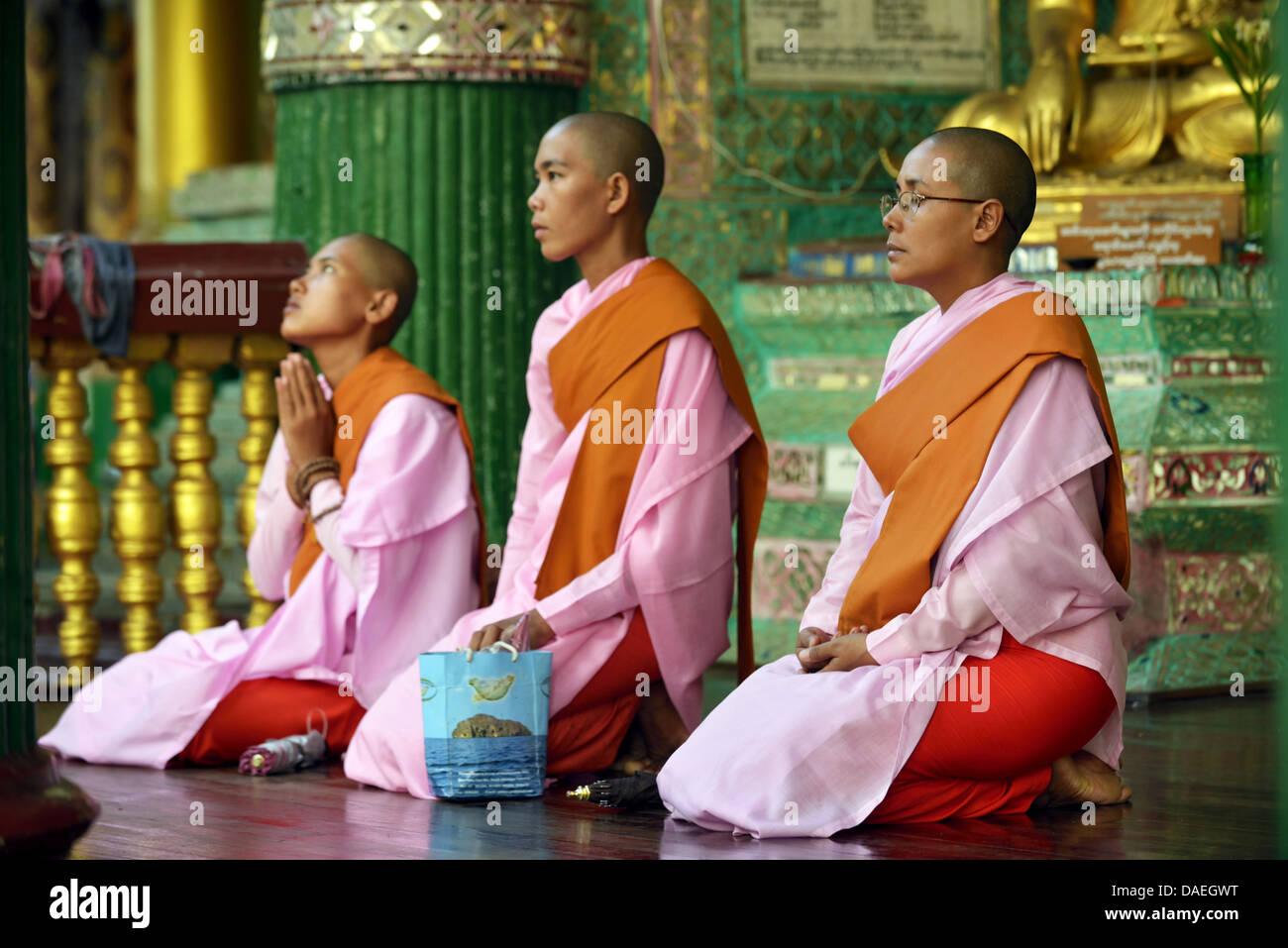three Buddhistic nuns sitting praying at the Shwedagon Pagoda, the most important sacral building and religious centre of the country, Burma, Yangon Stock Photo