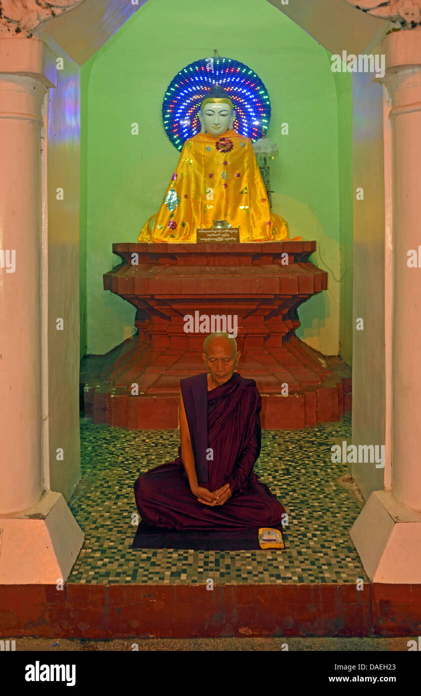 old monk sitting meditating in front of a Buddha statue at the Shwedagon Pagoda, the most important sacral building and religious centre of the country, Burma, Yangon Stock Photo