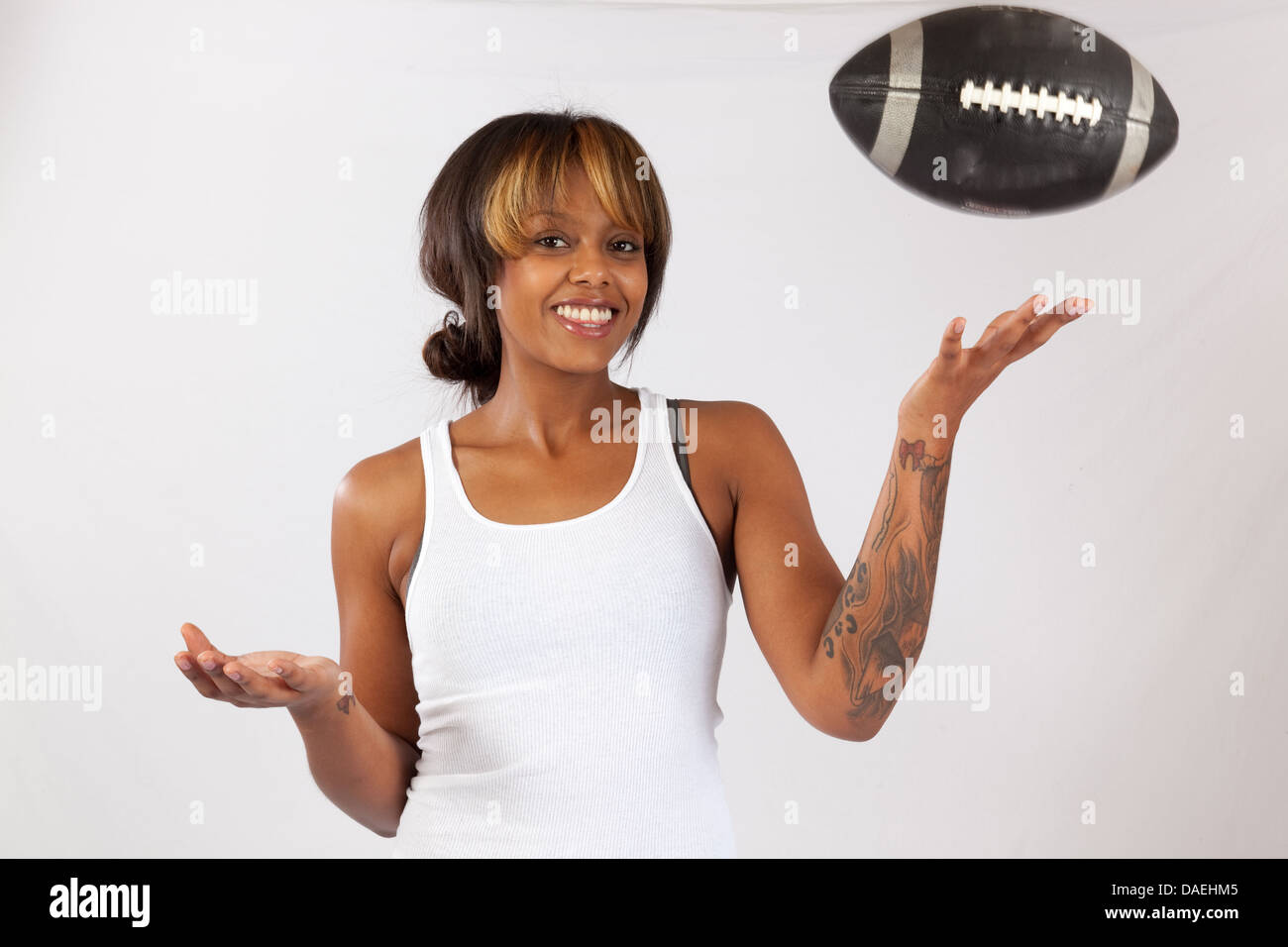 Pretty black woman in an undershirt tossing a football in the air and smiling at the camera with a happy smile Stock Photo