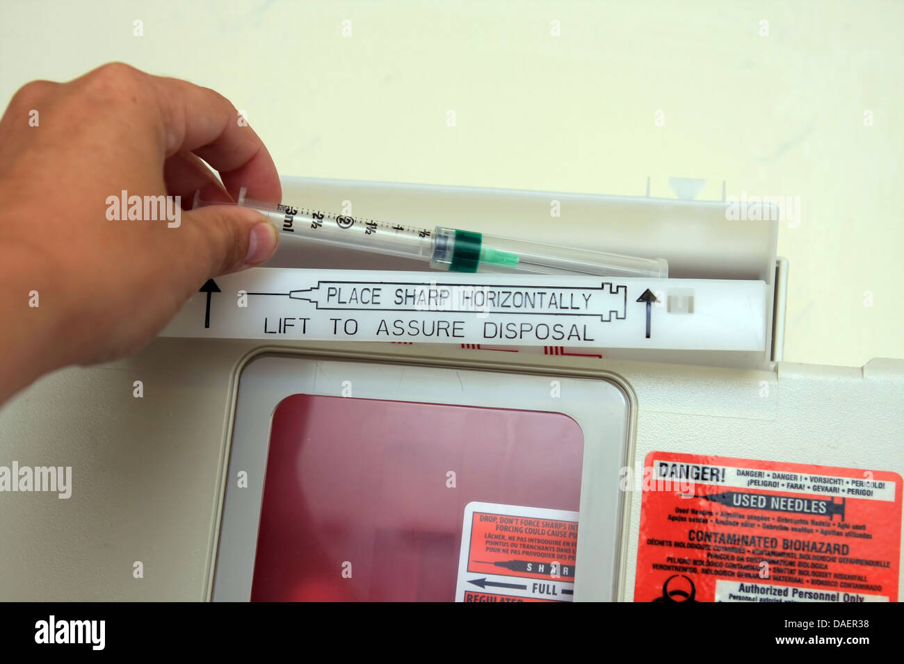 nurse hand placing used needle syringe into red sharps biohazard container Stock Photo