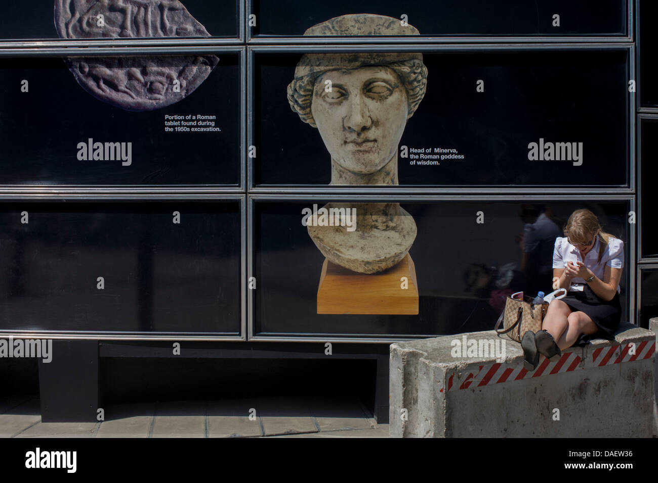 Walbrook Roman archeology Minerva Goddess figure and modern woman using her smartphone by a construction hoarding in the City of London. Stock Photo
