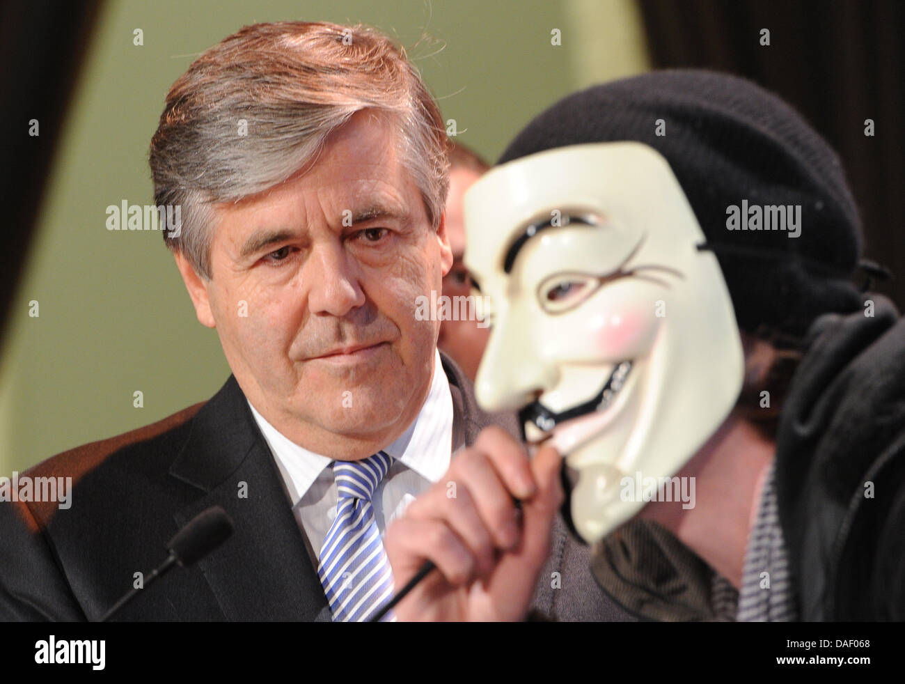 An Occupy activist wearing a Guy Fawkes mask interrupts Joseph Ackermann, CEO of Deutsche Bank, during his speech to the members' meeting of the Ehrbarer Kaufmann (Honorable Merchants) in Hamburg, Germany, 22 November 2011. Several activists of the Occupy movement disrupted the speech of the bank chief and stormed the podium at the chamber of commerce in Hamburg. Photo: MARCUS BRAN Stock Photo