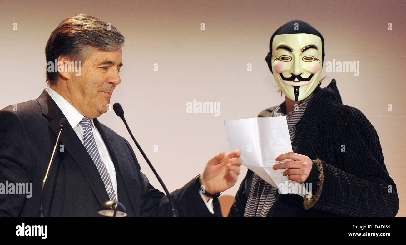 An Occupy activist wearing a Guy Fawkes mask interrupts Joseph Ackermann, CEO of Deutsche Bank, during his speech to the members' meeting of the Ehrbarer Kaufmann (Honorable Merchants) in Hamburg, Germany, 22 November 2011. Several activists of the Occupy movement disrupted the speech of the bank chief and stormed the podium at the chamber of commerce in Hamburg. Photo: MARCUS BRAN Stock Photo