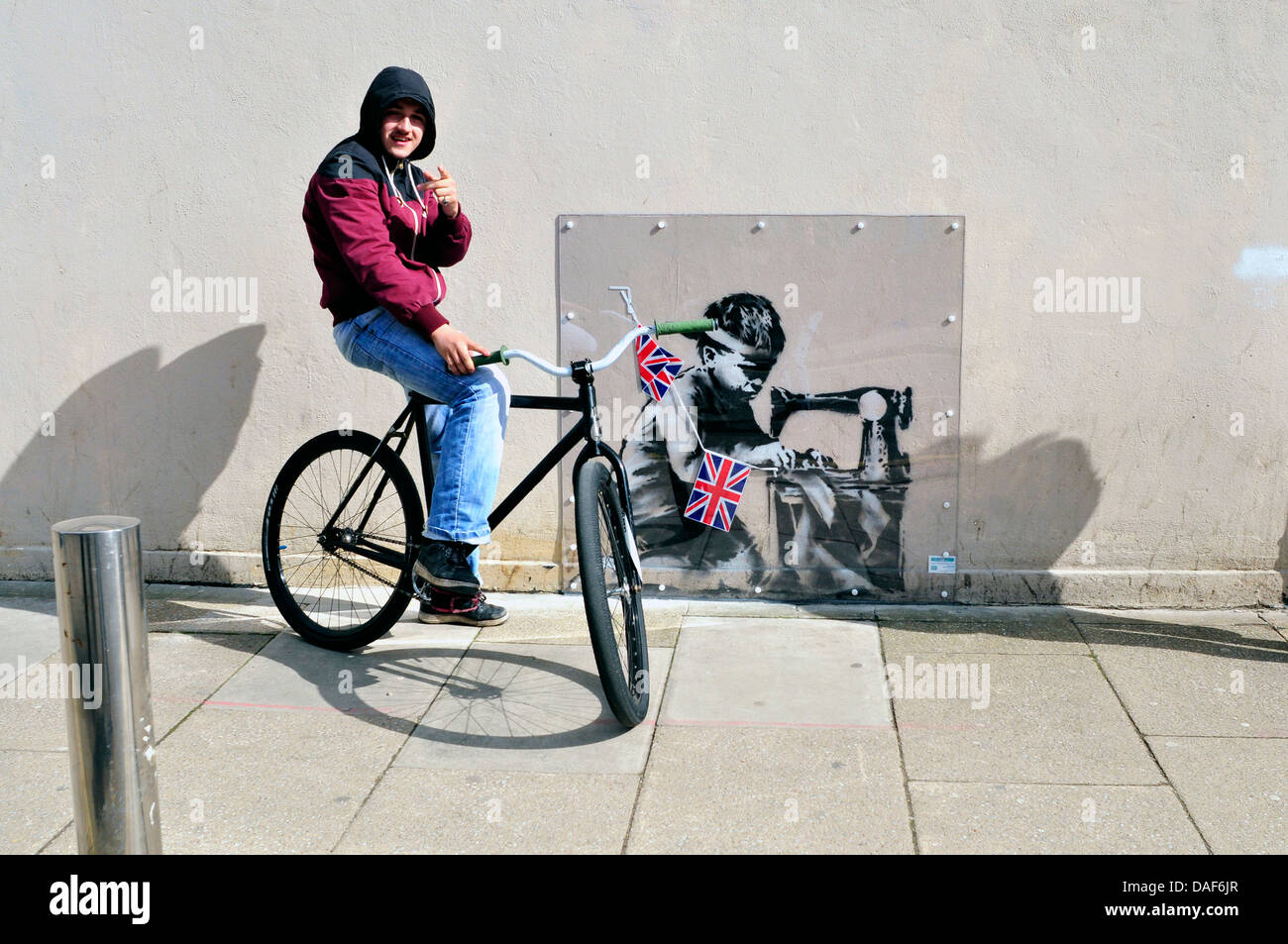 A local youth with a bicycle, stands next to Banksy's mural. Turnpike Lane, London, UK Stock Photo