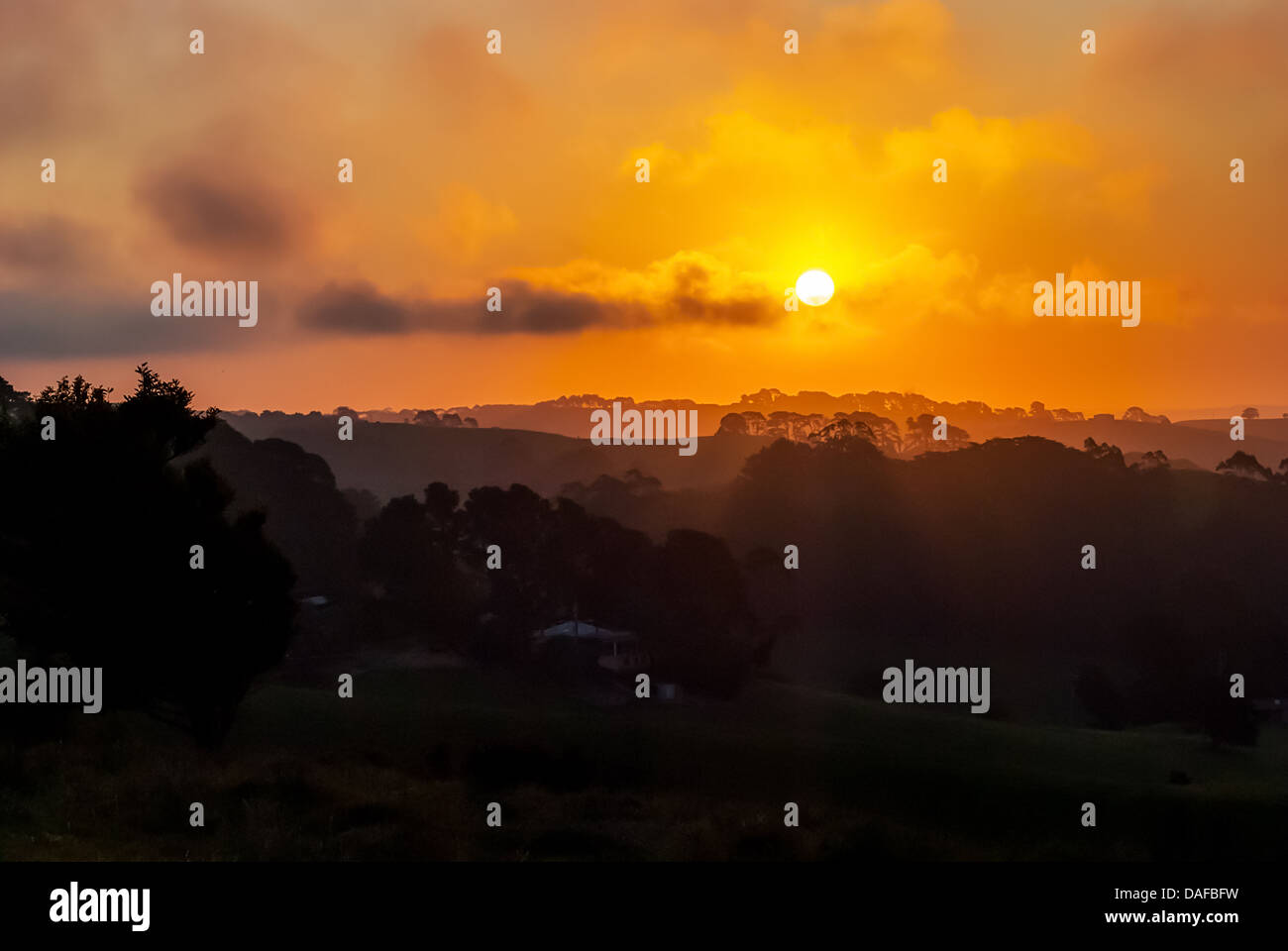 A fiery sunset silhouettes the rolling countryside and farmland of Gippsland in Victoria, Australia. Stock Photo