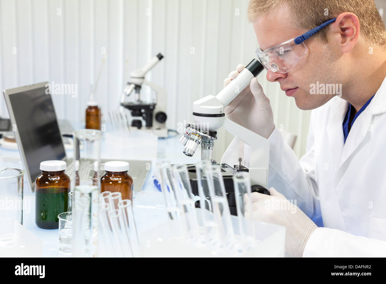 A male medical or scientific researcher or doctor using a microscope in ...