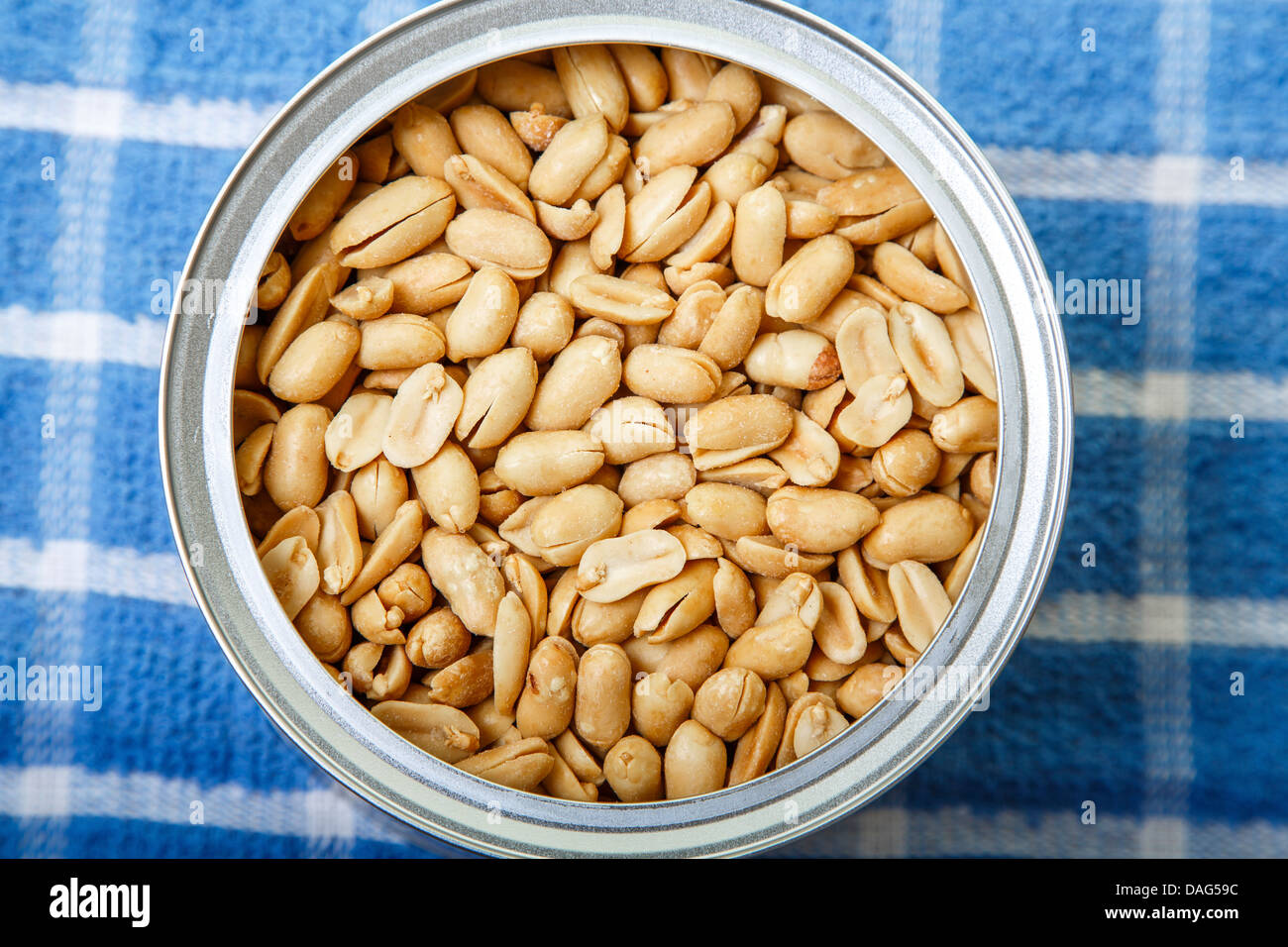 Salted peanuts in a round can on a blue and white plaid placemat Stock Photo