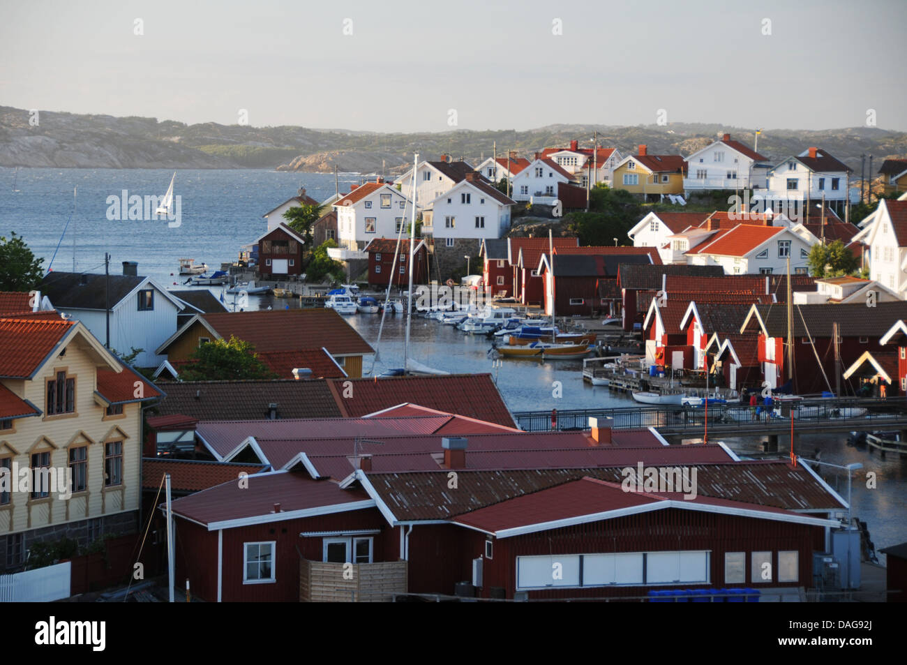 Sailboat outside harbor filled with boathouses, homes and yachts on island of Gullholmen on West