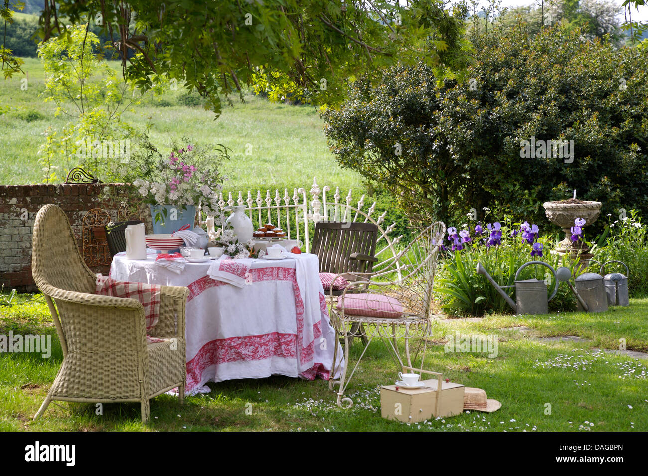 Lloyd Loom chair beside table with white cloth edged with red on lawn in country garden in summer Stock Photo
