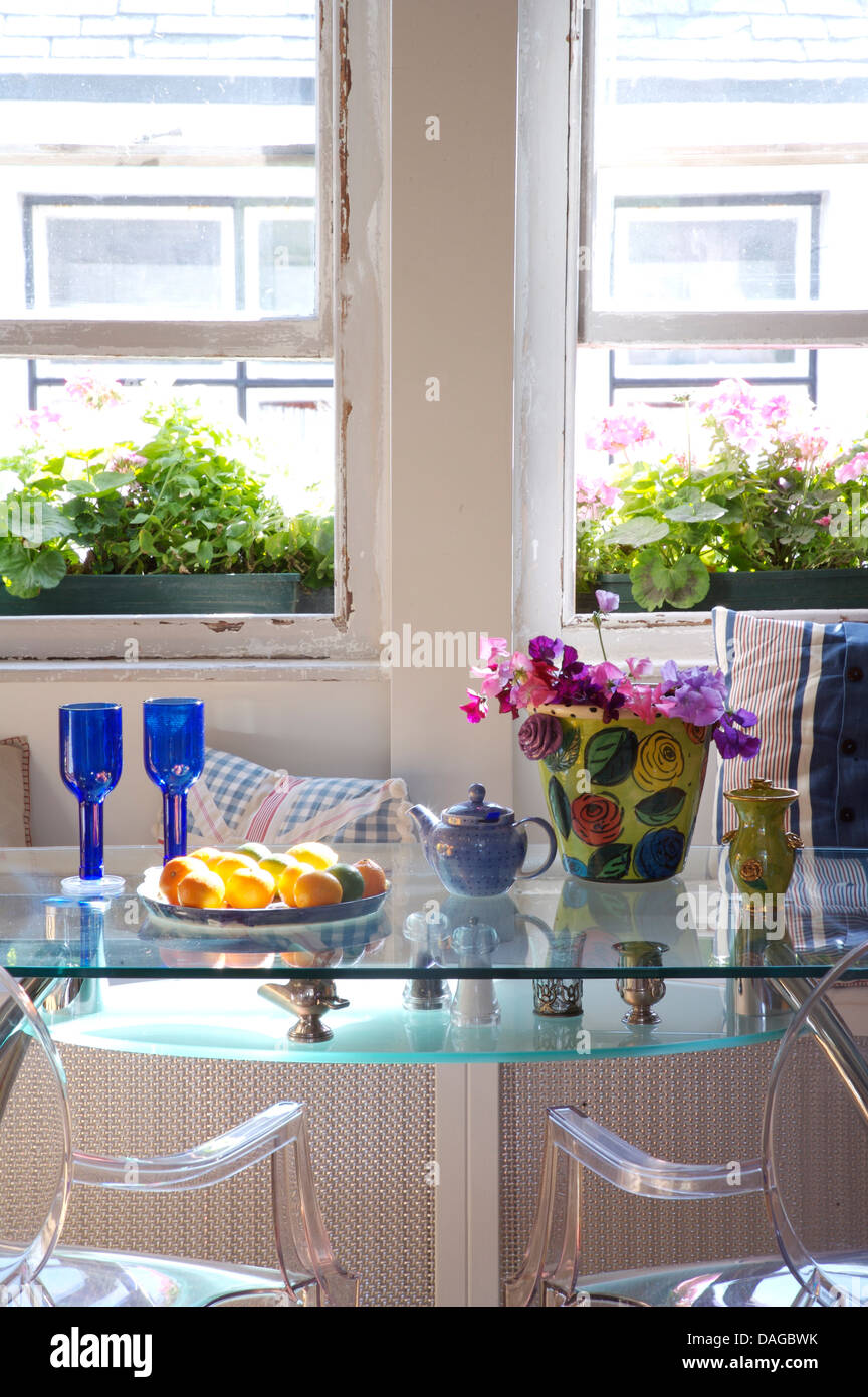 Dining room with blue glasses and vase of sweet peas on glass topped table with pair of Philippe Starck 'Ghost' chairs Stock Photo