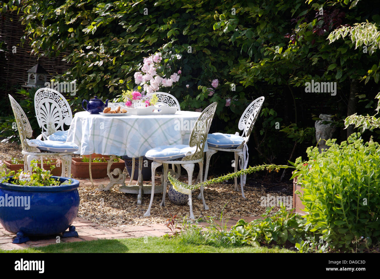 White wrought iron chairs and table with checked cloth set for tea in country garden in summer Stock Photo