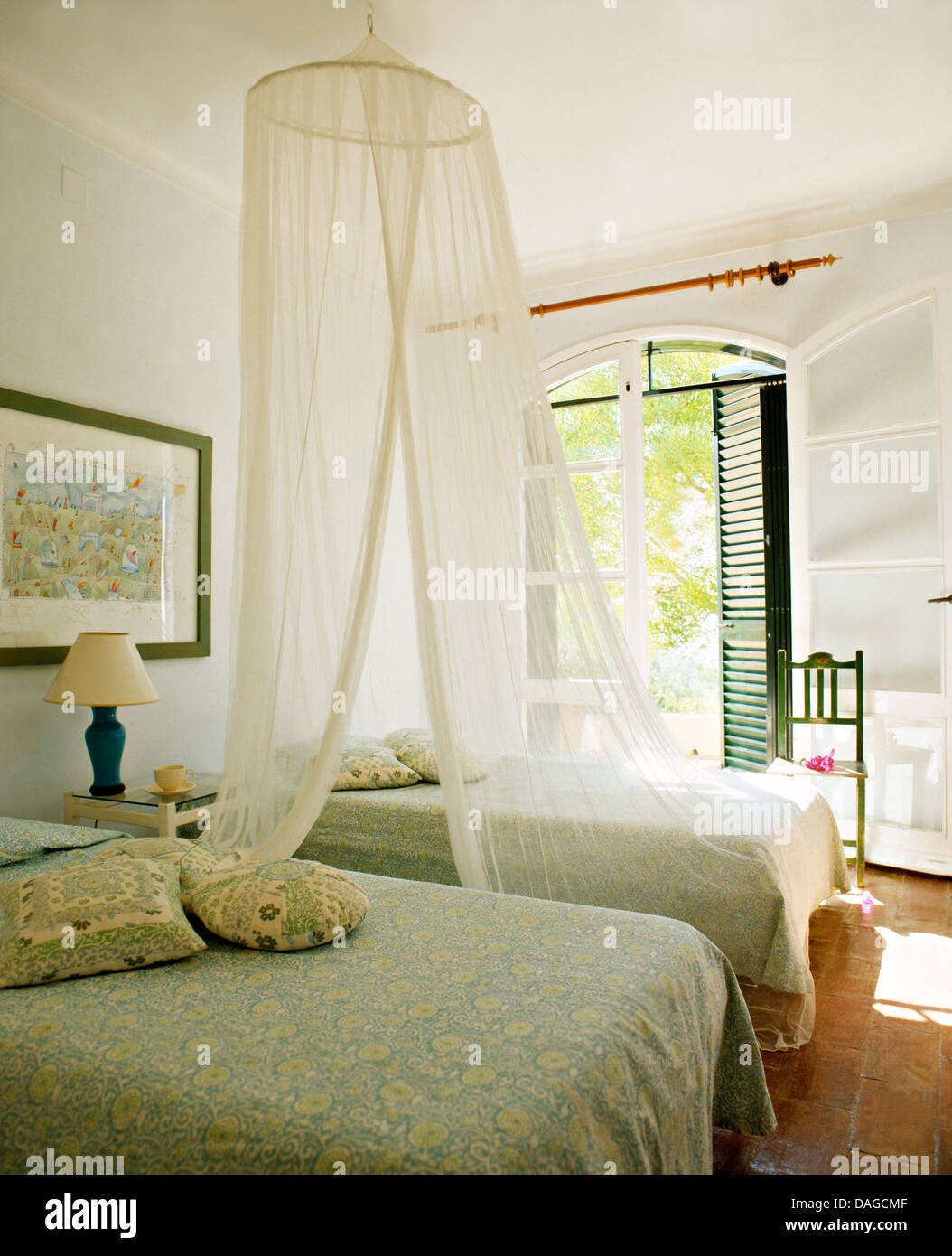 Mosquito net above twin beds with pale green bedspreads in white
