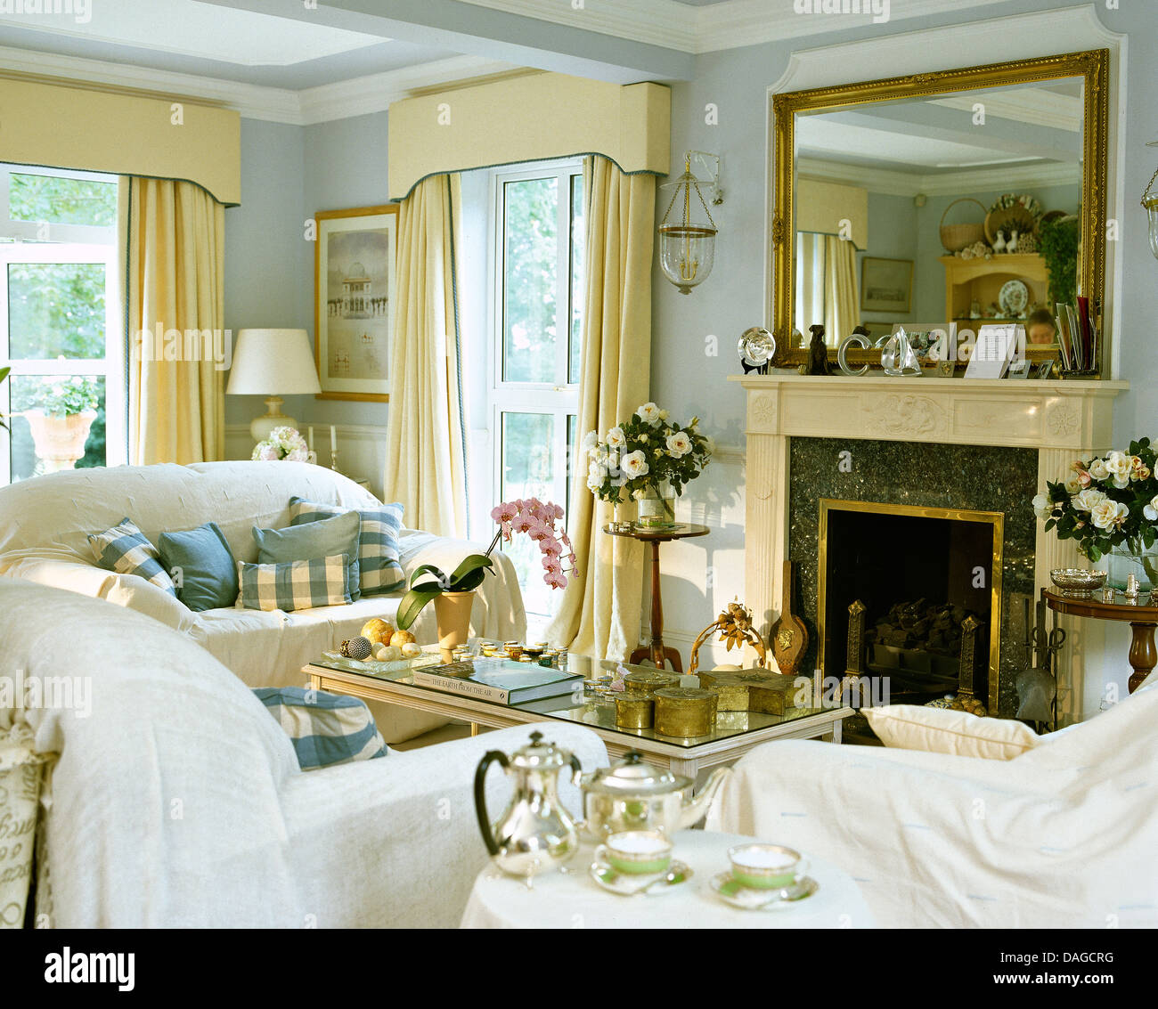 White throws on sofas in pale blue living room with large mirror above  fireplace and cream drapes on windows Stock Photo - Alamy