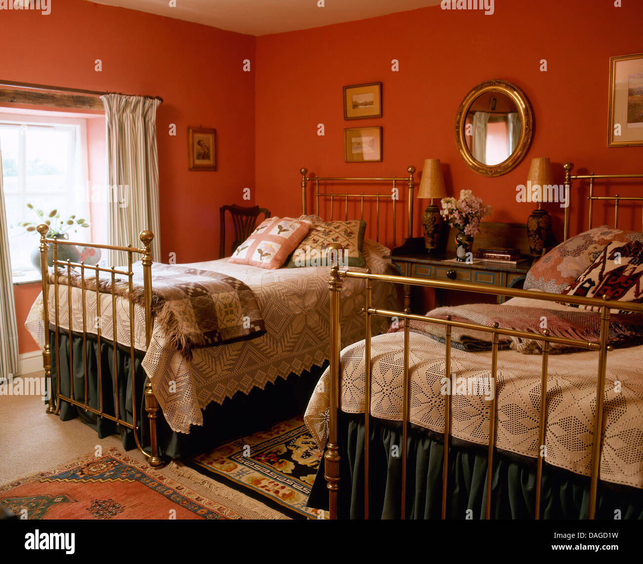 Cushions and cream covers on twin antique brass beds in red cottage