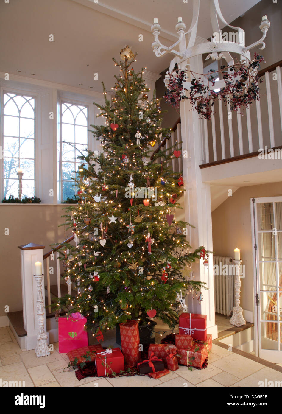 Gift Wrapped Presents In Bright Red Paper Below Tall Decorated Christmas Tree In Country Hall With White Metal Chandelier Gift Wrapped Presents In Bright Red Paper Below Tall Decorated Christmas Tree In Country Hall With White Metal Chandelier