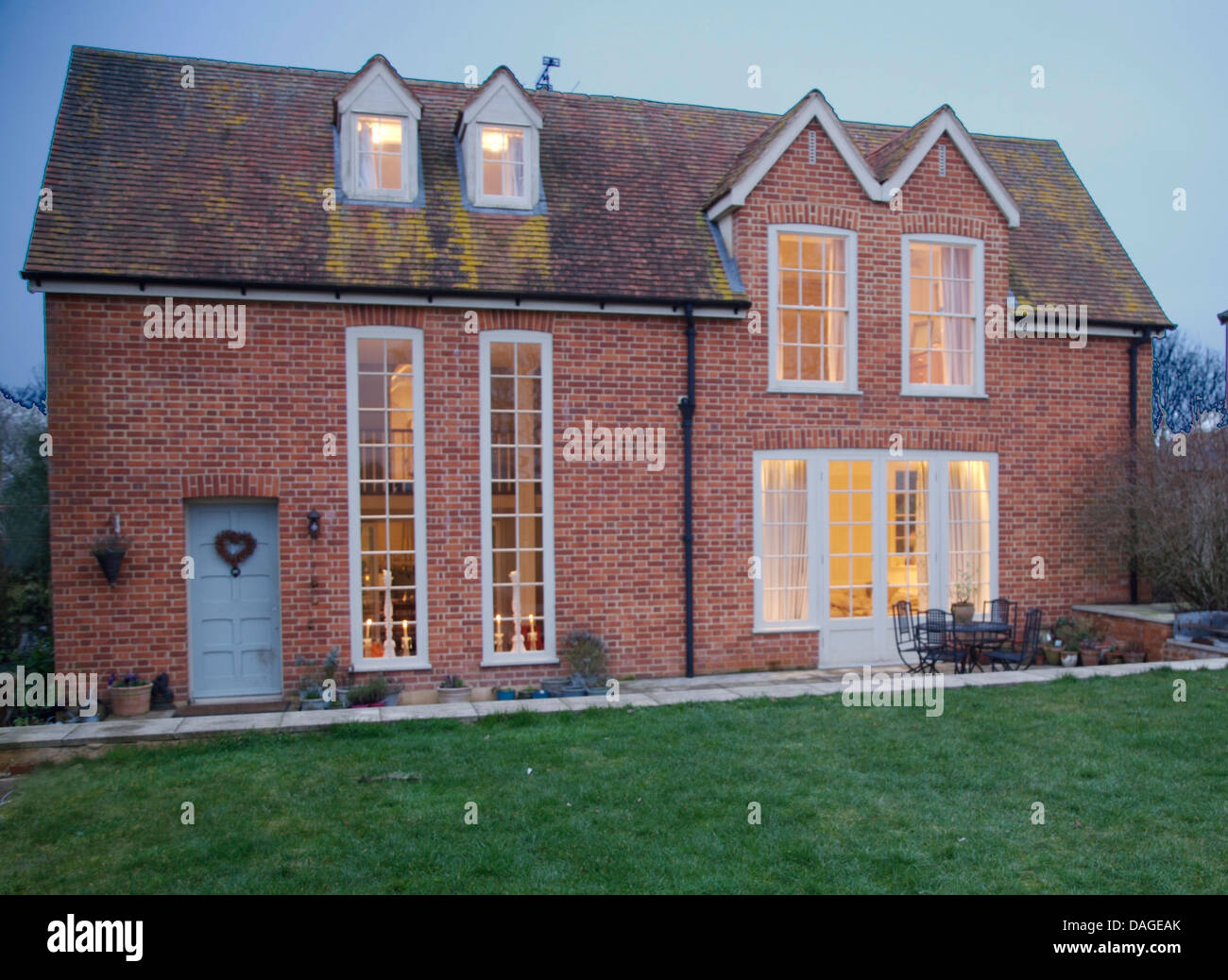 Exterior of brick built country house with tall, narrow windows beside blue front door, lit in early evening Stock Photo