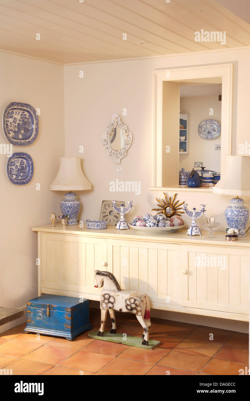 Blue+white pottery on white painted sideboard below hatch in country  dining room with old blue wooden chest and wooden horse Stock Photo