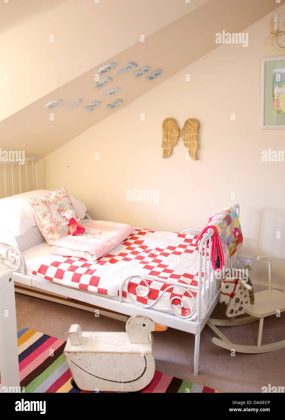 Wrought iron single bed with red+white patchwork quilt in child's attic bedroom with wooden sit-on duck and horse Stock Photo