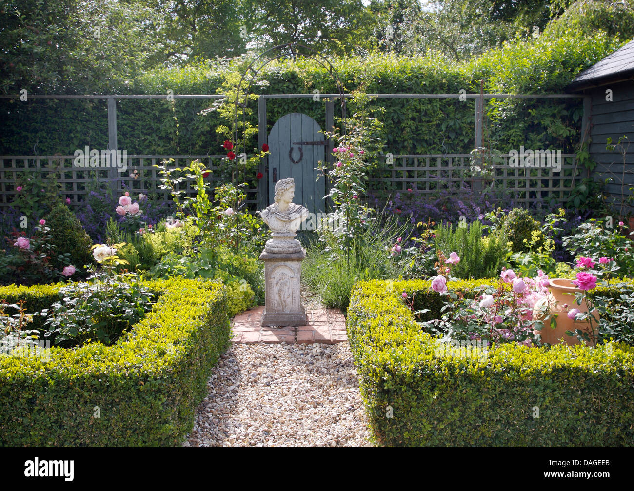 Classical statue on plinth in center of formal country garden with gravel path and roses in beds enclosed by low box hedges Stock Photo