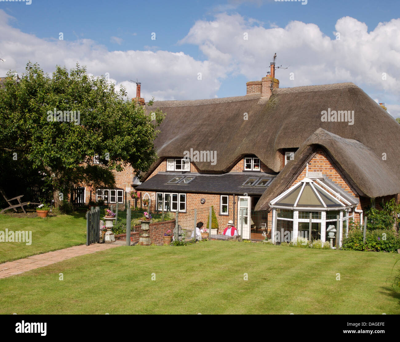 Lawn in front of large country cottage with thatched roof and conservatory extension Stock Photo