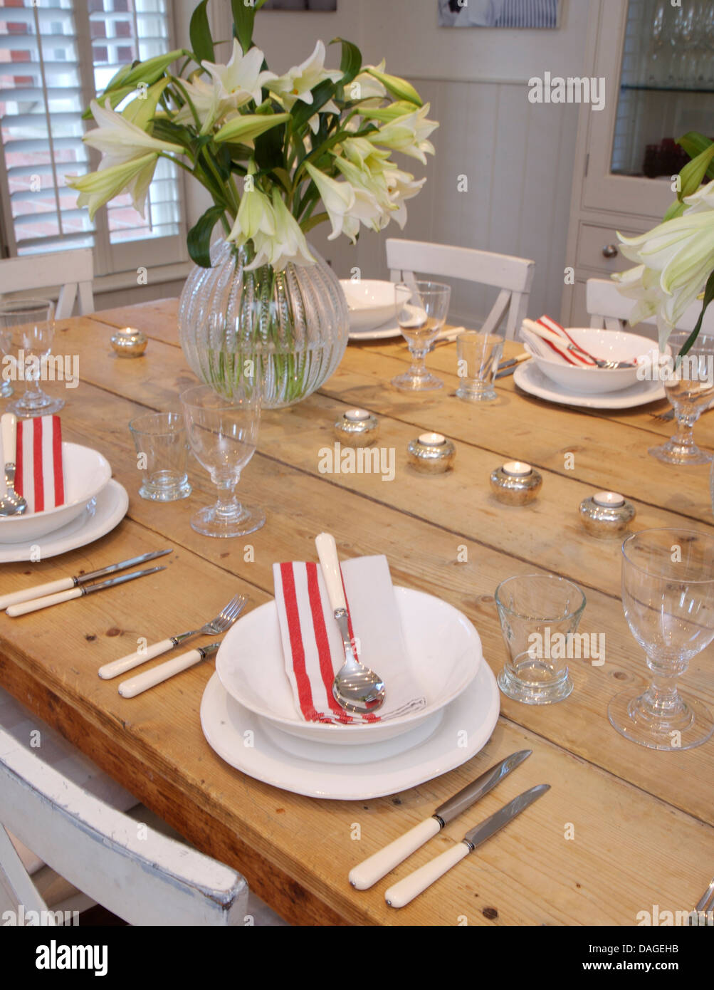 Close-up of pine table set for dinner with white crockery and vase of white lilies in country dining room Stock Photo