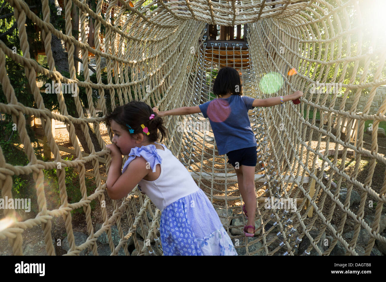 Two girls cross a suspended bridge made of ropes. Stock Photo