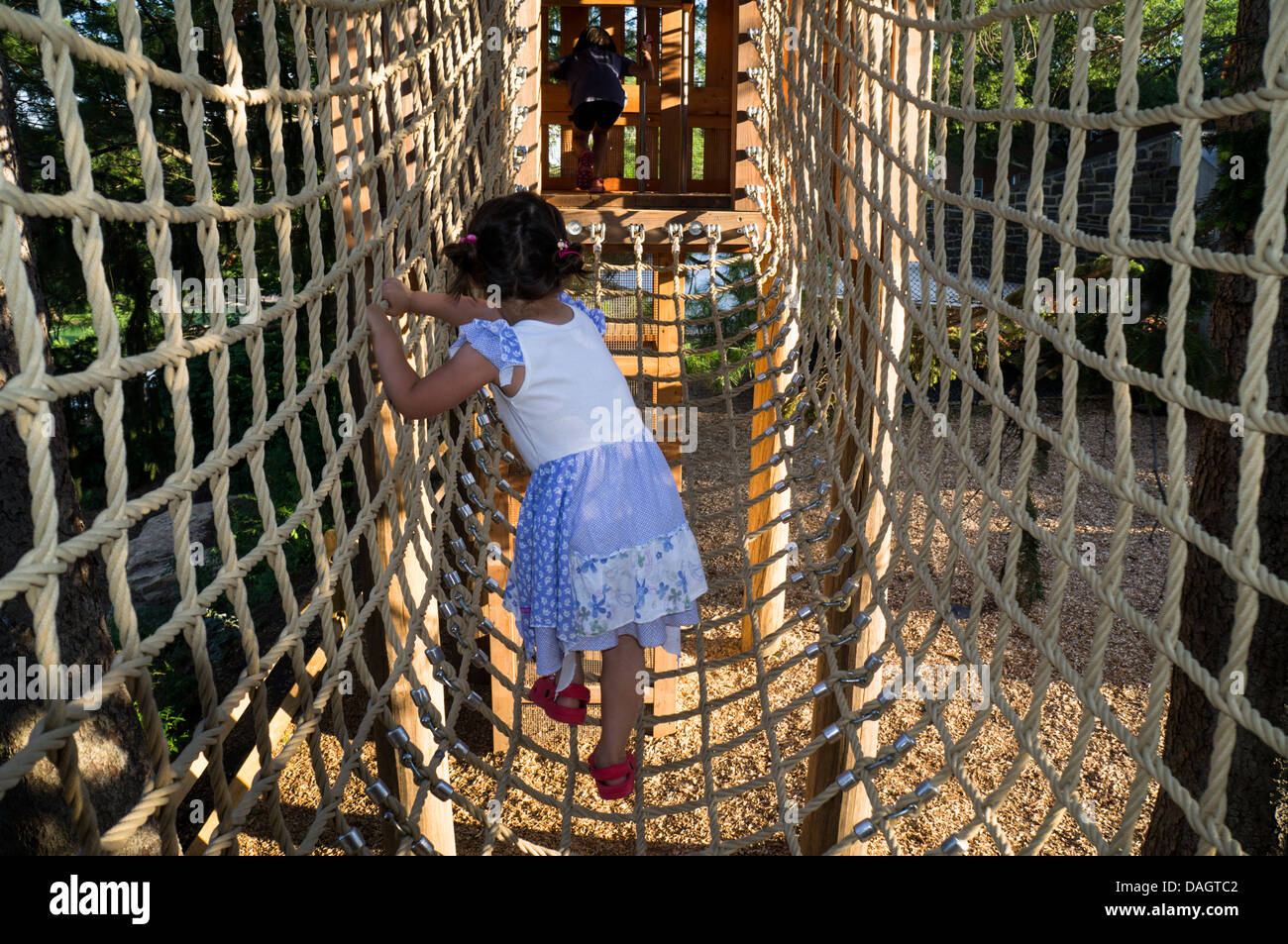 A girl crosses a suspended bridge made of ropes. Stock Photo