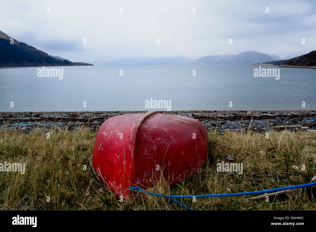 Horizontal image of an upturned red boat on shore of Scottish loch Stock Photo