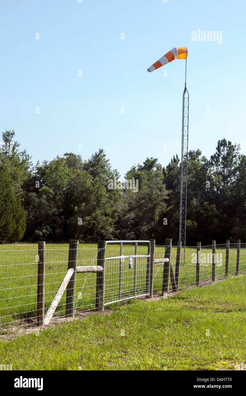 Fenced entry gate protects rural landing strip serving the Cedar Key, Florida area.  A wind sock is mounted on a metal mast. Stock Photo