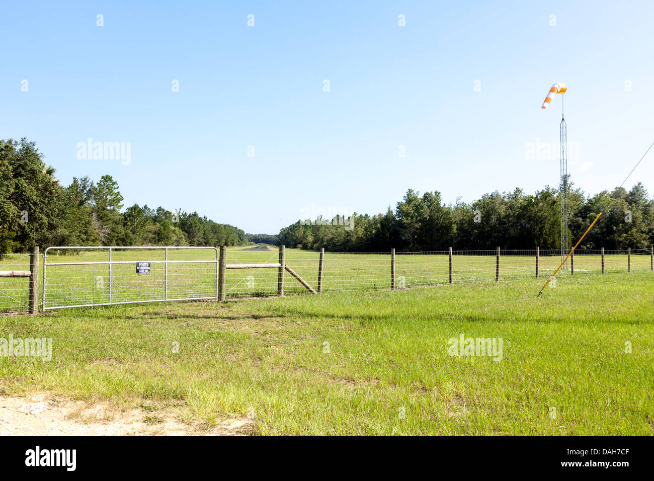 Fenced entry gate protects grass landing strip beyond in Cedar Key, Florida area.  A wind sock is mounted on a metal mast. Stock Photo