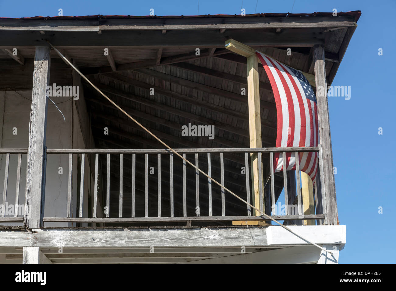 Old Glory American flag hangs vertically between corner posts supporting a wide veranda. Stock Photo