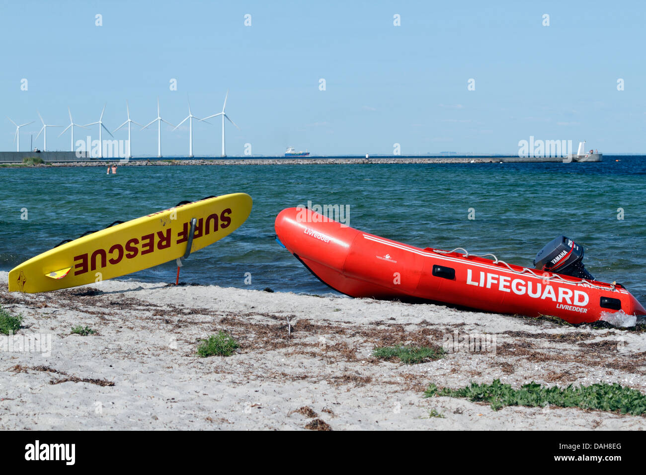 Lifeguard rescue board and inflatable boat on the beach at Kastrup, Copenhagen. Middelgrunden offshore wind park in background. Stock Photo
