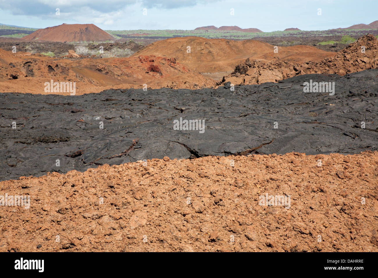 Hardened younger black pahoehoe lava flow on top of older oxidized and fragmented red aa lava flow with volcanic cones on Santiago Island, Galapagos Stock Photo