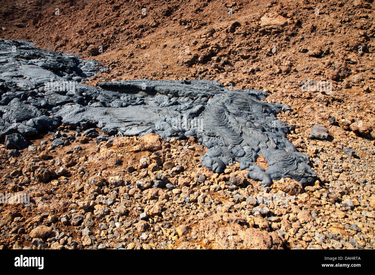 Hardened dark pahoehoe lava flow on top of older oxidized and fragmented red aa lava Stock Photo