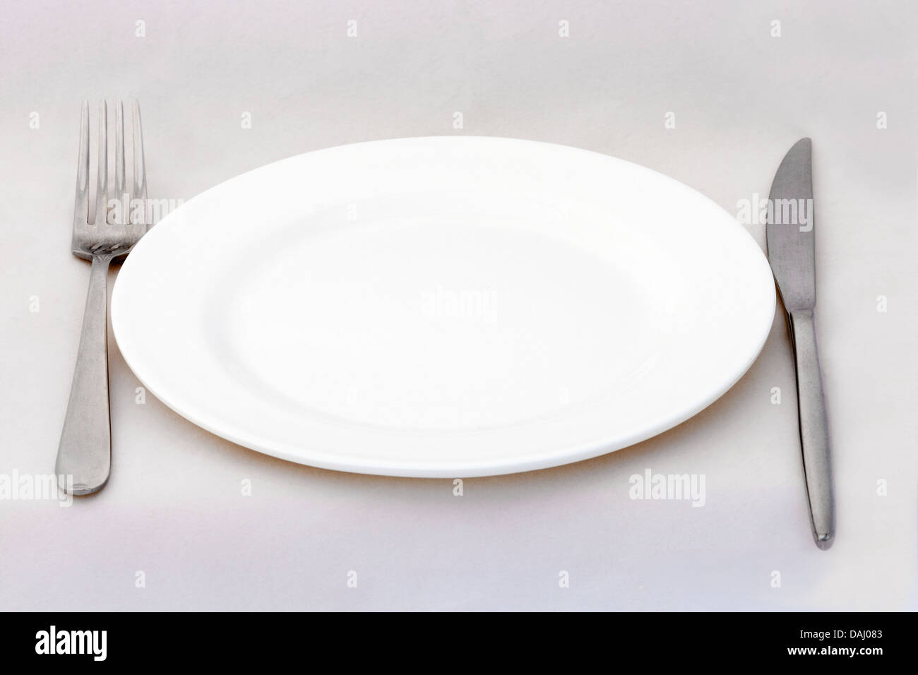 Dining plate with fork and knife on white surface Stock Photo
