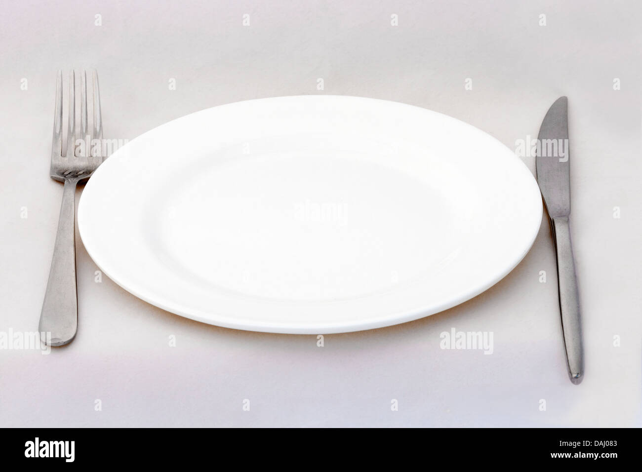 Dining plate with fork and knife on white surface Stock Photo - Alamy